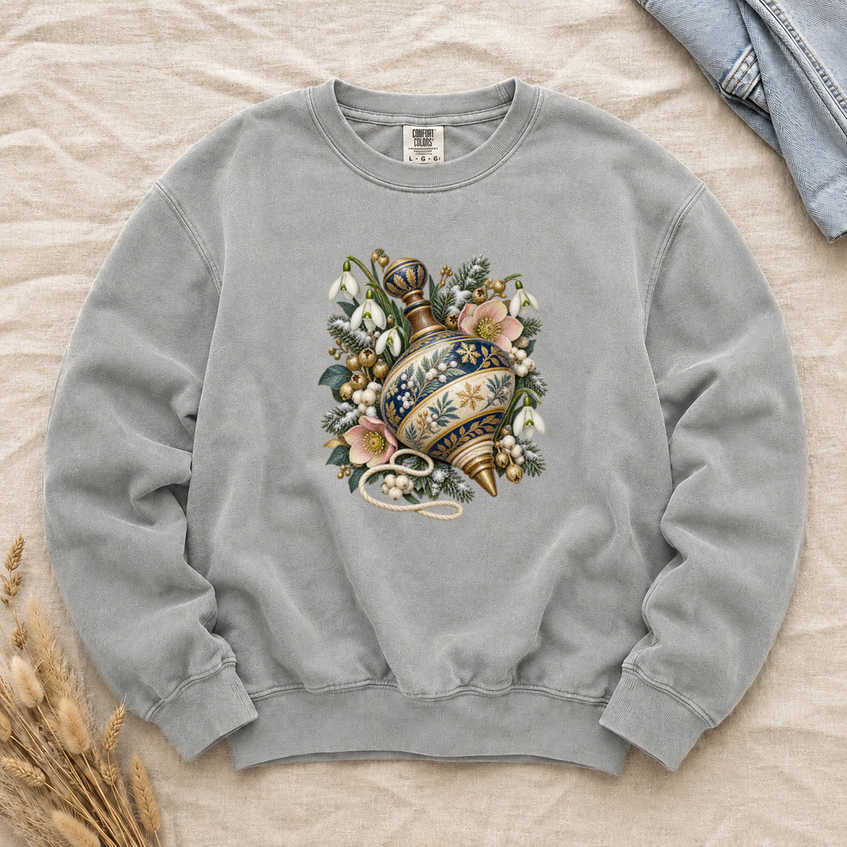 Vintage Spinning Top & Winter Florals Sweatshirt in Grey — an ornate spinning top in deep blue, cream and gold, resting among evergreen sprigs, white snowdrops, pink flowers and pale berries, a loose cord curling beneath its tip