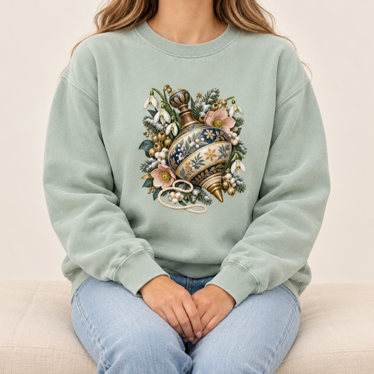 Spinning top winter sweatshirt, relaxed unisex fit, adult sizes S to 3XL — a deep blue, cream and gold spinning top among evergreen sprigs, white snowdrops, pink flowers and pale berries