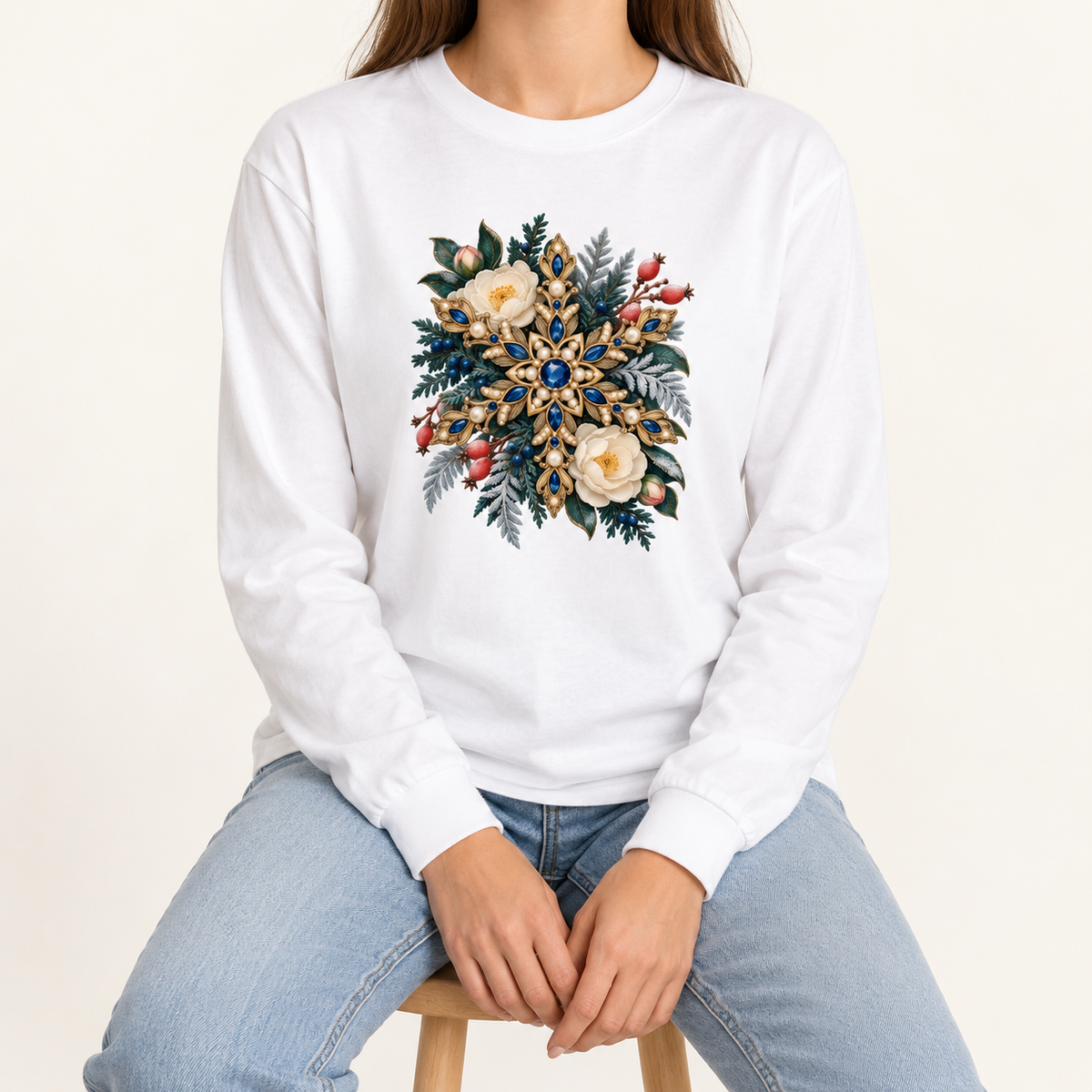 White long sleeve tee showing the printed gemstone and pearl detail at full size, printed and not embroidered — a golden snowflake set with deep blue gemstones and pearls among cream flowers and frosted evergreen
