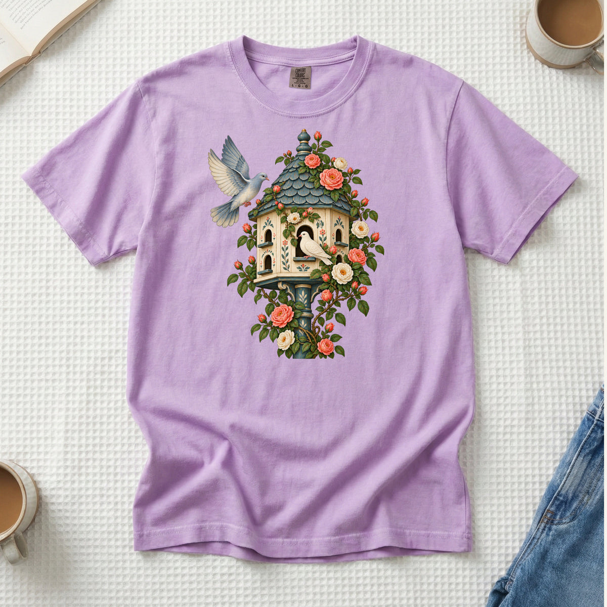Whoever Gets There First T-Shirt in Orchid — a gentle storybook purple against the green leaves