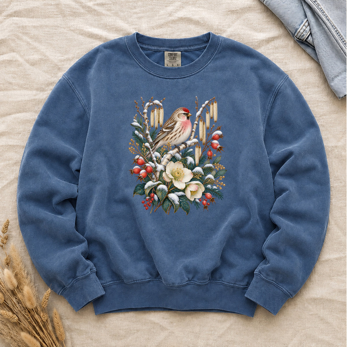 Winter Finch & Botanical Sweatshirt in Blue Jean — a small brown finch with rosy red markings perched among branches hung with golden catkins, above snow-dusted evergreen, red berries and cream flowers