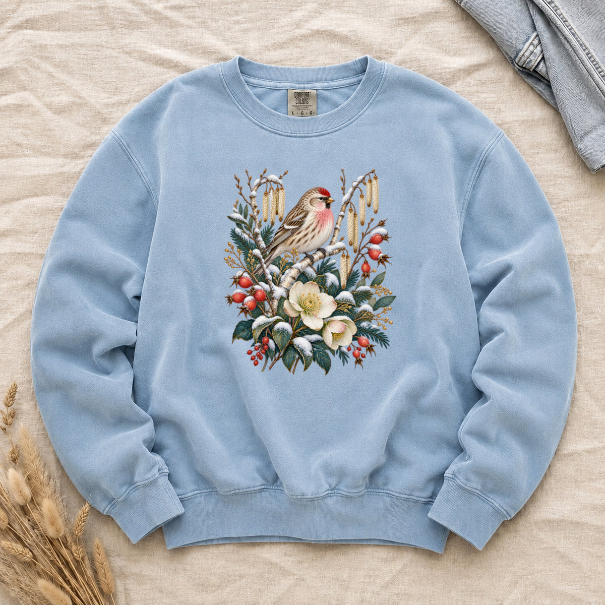 Winter Finch & Botanical Sweatshirt in Chambray — a small brown finch with rosy red markings perched among branches hung with golden catkins, above snow-dusted evergreen, red berries and cream flowers