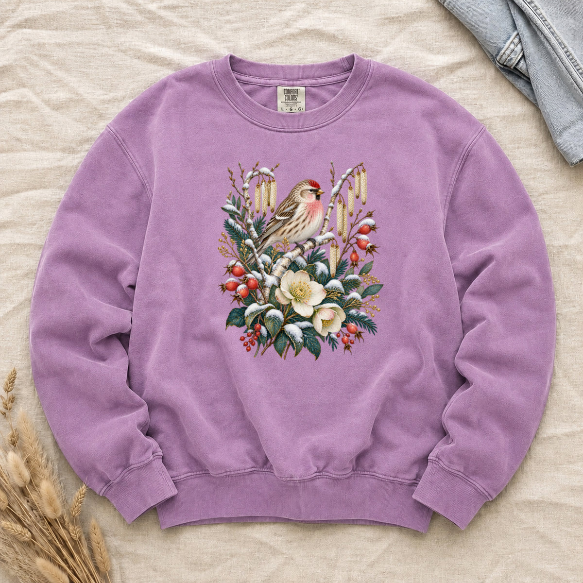 Winter Finch & Botanical Sweatshirt in Orchid — a small brown finch with rosy red markings perched among branches hung with golden catkins, above snow-dusted evergreen, red berries and cream flowers