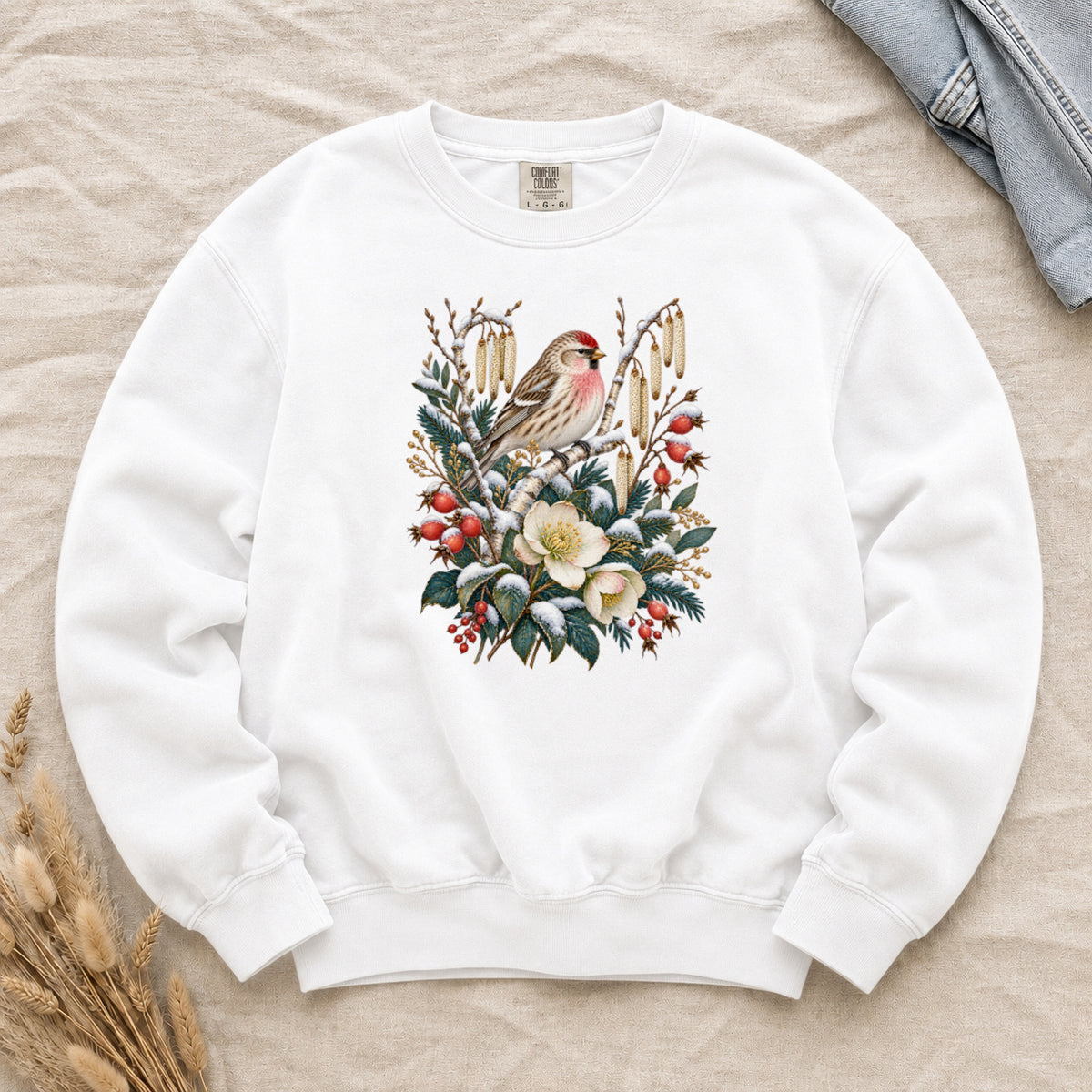 Winter Finch & Botanical Sweatshirt in White — a small brown finch with rosy red markings perched among branches hung with golden catkins, above snow-dusted evergreen, red berries and cream flowers