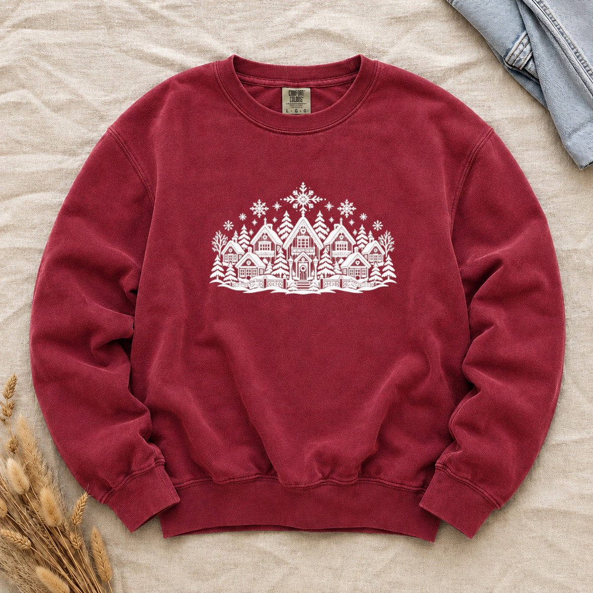 Winter Village White Line Art Sweatshirt in Crimson — the white line drawing of houses, pines and falling snow on a deep red garment-dyed crewneck