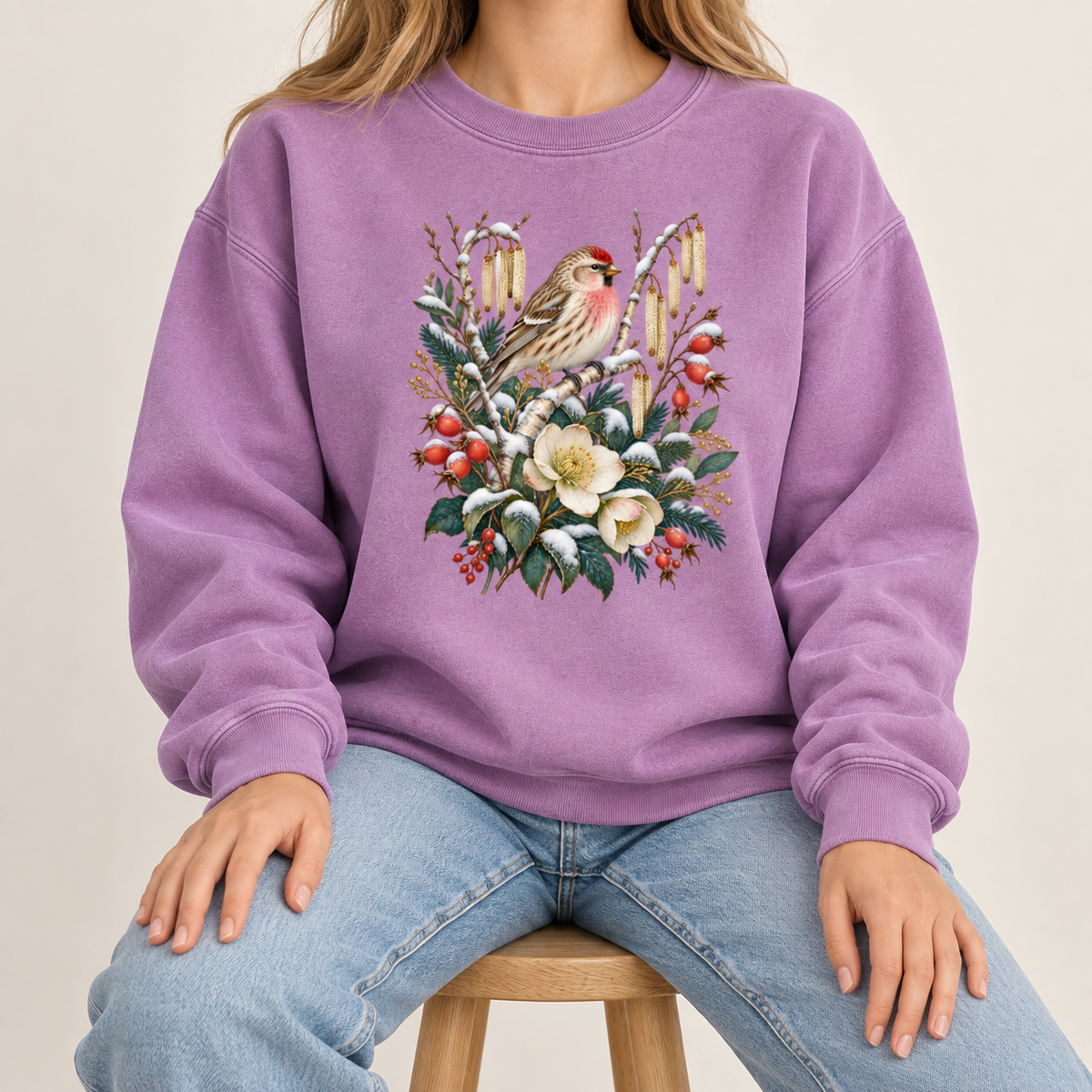 Winter finch botanical sweatshirt, large front-centered print, no lettering — a small brown finch with rosy red markings above snow-dusted evergreen, red berries and cream flowers