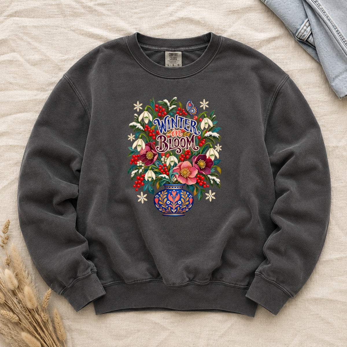 Winter in Bloom folk bouquet sweatshirt in Pepper, a dark charcoal garment-dyed Comfort Colors crewneck, printed with white snowdrops, crimson hellebores, pink blooms and red winterberry in a blue-and-white folk vase