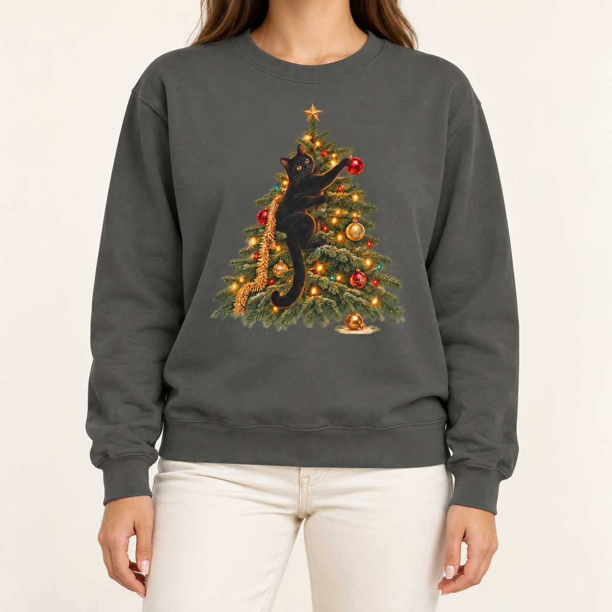 Black cat Christmas sweatshirt in Pepper worn with jeans – black cat climbing a lit Christmas tree, reaching for a red ornament, Comfort Colors crewneck