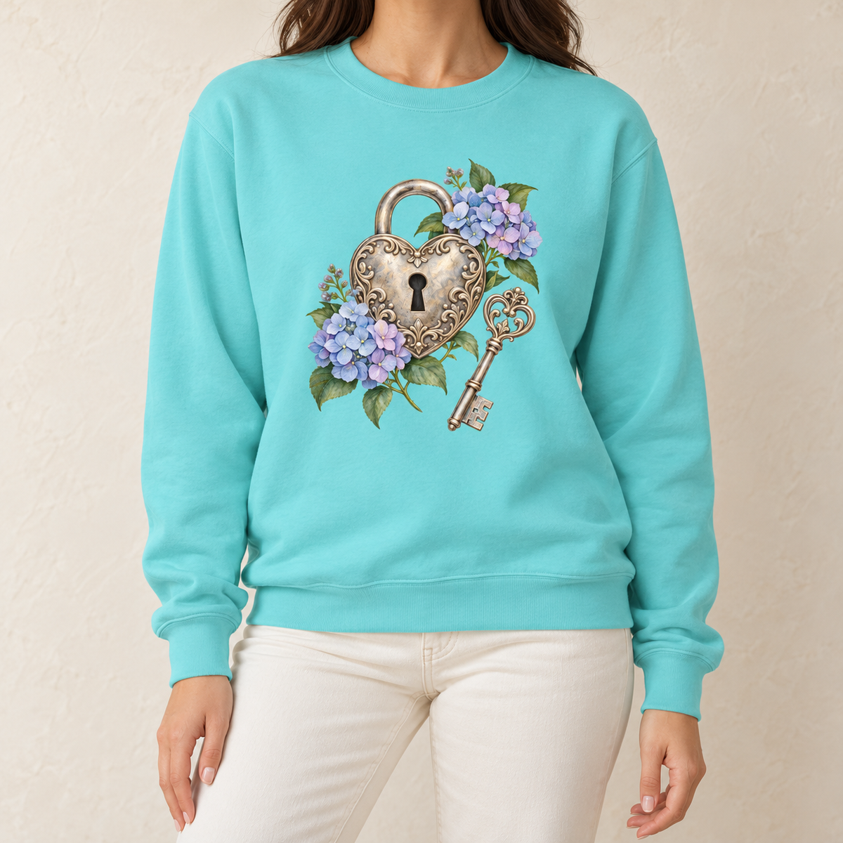 Detailed watercolor of a silver filigree heart padlock and skeleton key among blue and purple hydrangeas, printed large and centered on the front of a Chalky Mint pale mint 9.5 oz garment-dyed Comfort Colors 1566 sweatshirt, worn by a model