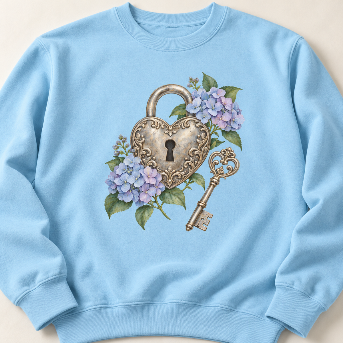 Detailed watercolor of a silver filigree heart padlock and skeleton key among blue and purple hydrangeas, printed large and centered on the front of a Chambray light blue 9.5 oz garment-dyed Comfort Colors 1566 sweatshirt, shown flat