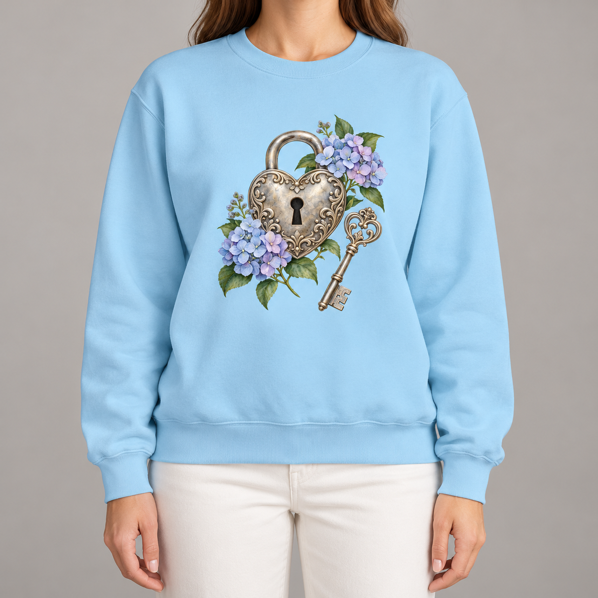 Detailed watercolor of a silver filigree heart padlock and skeleton key among blue and purple hydrangeas, printed large and centered on the front of a Chambray light blue 9.5 oz garment-dyed Comfort Colors 1566 sweatshirt, worn by a model