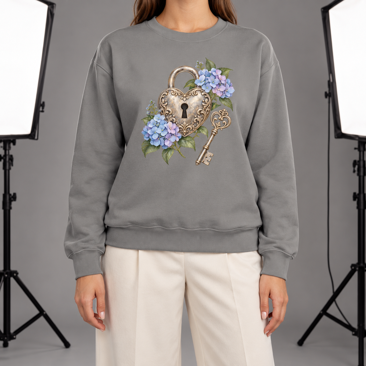 Detailed watercolor of a silver filigree heart padlock and skeleton key among blue and purple hydrangeas, printed large and centered on the front of a Grey 9.5 oz garment-dyed Comfort Colors 1566 sweatshirt, shown on a mannequin