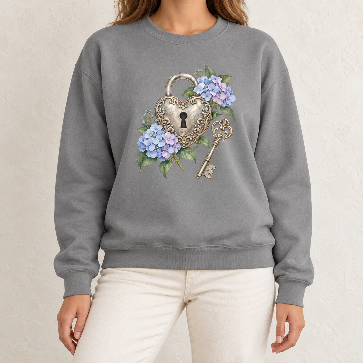 Detailed watercolor of a silver filigree heart padlock and skeleton key among blue and purple hydrangeas, printed large and centered on the front of a Grey 9.5 oz garment-dyed Comfort Colors 1566 sweatshirt, worn by a model