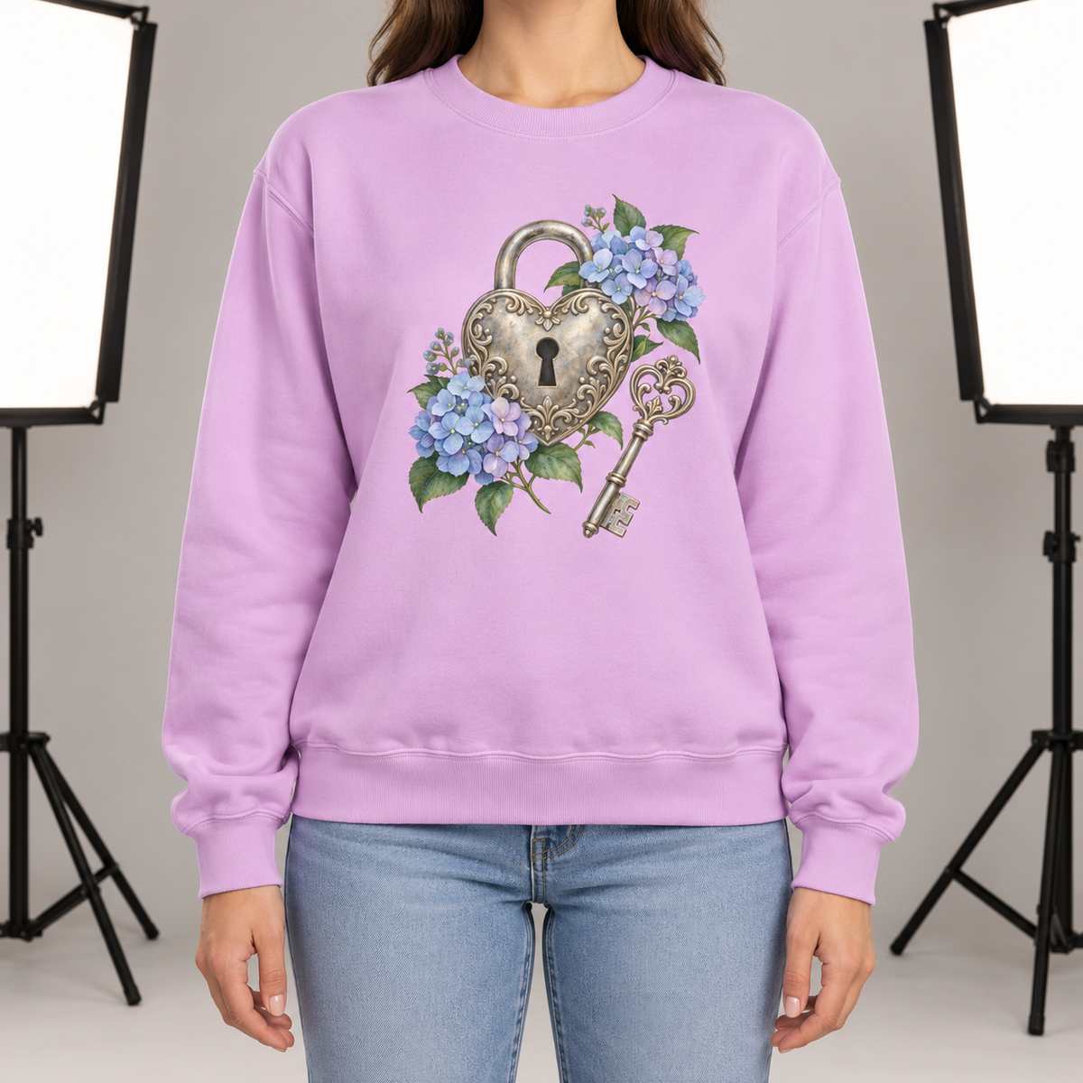 Detailed watercolor of a silver filigree heart padlock and skeleton key among blue and purple hydrangeas, printed large and centered on the front of an Orchid soft lilac 9.5 oz garment-dyed Comfort Colors 1566 sweatshirt, worn by a model