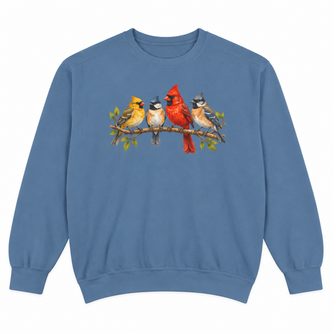 Front view of a Blue Jean Comfort Colors 1566 crewneck sweatshirt with four colorful songbirds — cardinal pair, chickadee and bluebird — on a leafy branch printed on the chest, no text, laid flat