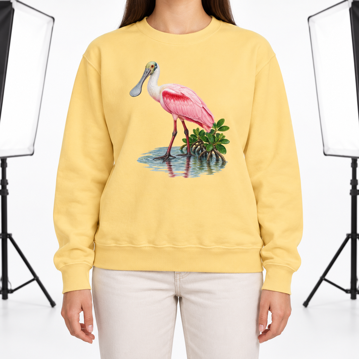 Woman wearing a Butter Comfort Colors 1566 crewneck sweatshirt with a roseate spoonbill wading in mangrove water printed on the chest, no text