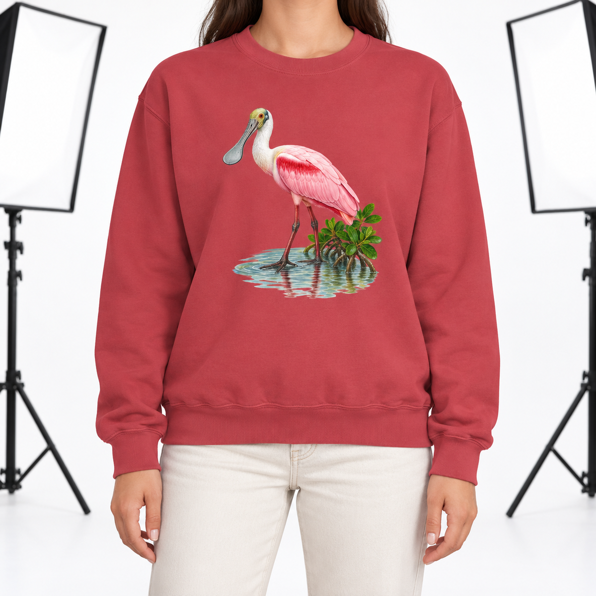Woman wearing a Crimson Comfort Colors 1566 crewneck sweatshirt with a roseate spoonbill wading in mangrove water printed on the chest, no text