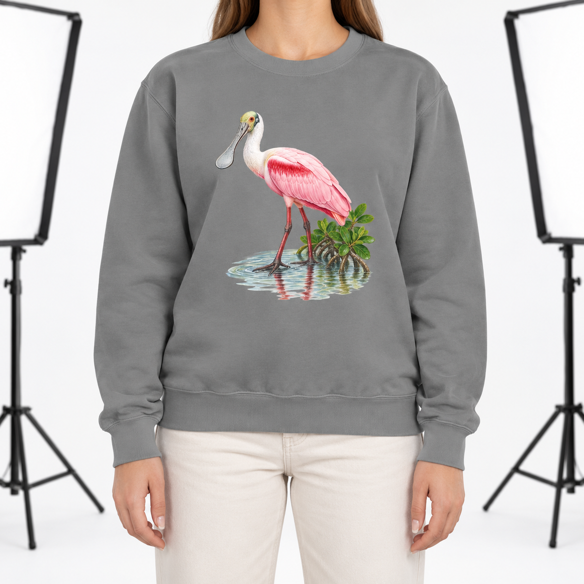 Woman wearing a Grey Comfort Colors 1566 crewneck sweatshirt with a roseate spoonbill wading in mangrove water printed on the chest, no text
