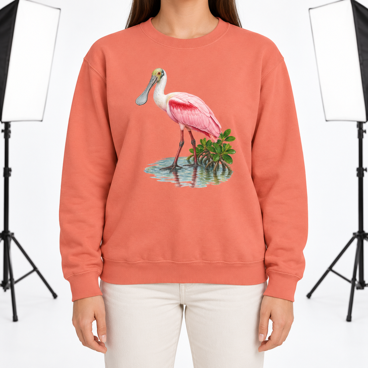 Woman wearing a Terracotta Comfort Colors 1566 crewneck sweatshirt with a roseate spoonbill wading in mangrove water printed on the chest, no text