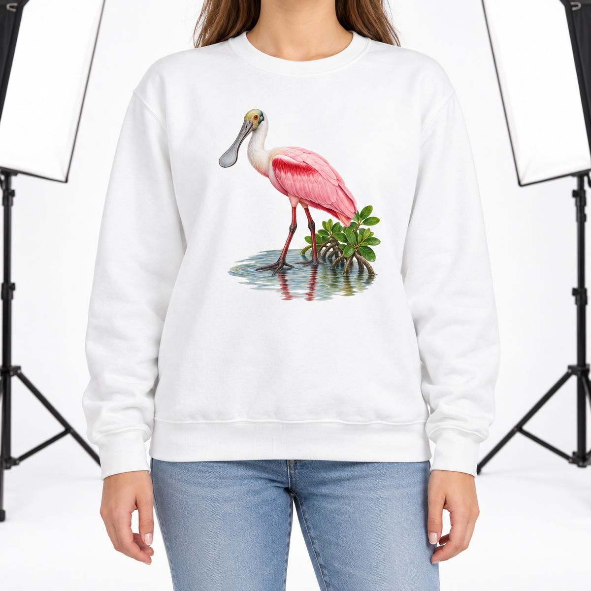 Woman wearing a White Comfort Colors 1566 crewneck sweatshirt with a roseate spoonbill wading in mangrove water printed on the chest, no text