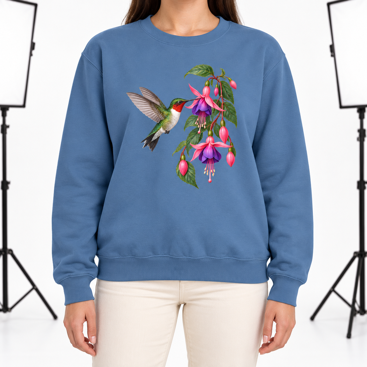 Woman wearing the Ruby-throated Hummingbird & Fuchsia sweatshirt in Blue Jean, a hummingbird hovering at a spray of pink and purple fuchsia, large centered chest print