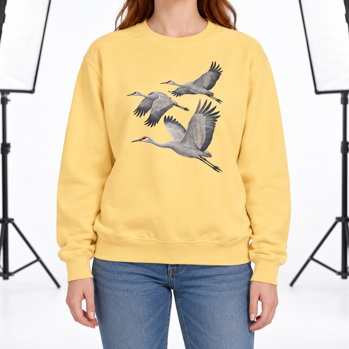 Woman wearing a Butter Comfort Colors 1566 crewneck sweatshirt with three sandhill cranes in flight printed on the chest, no text