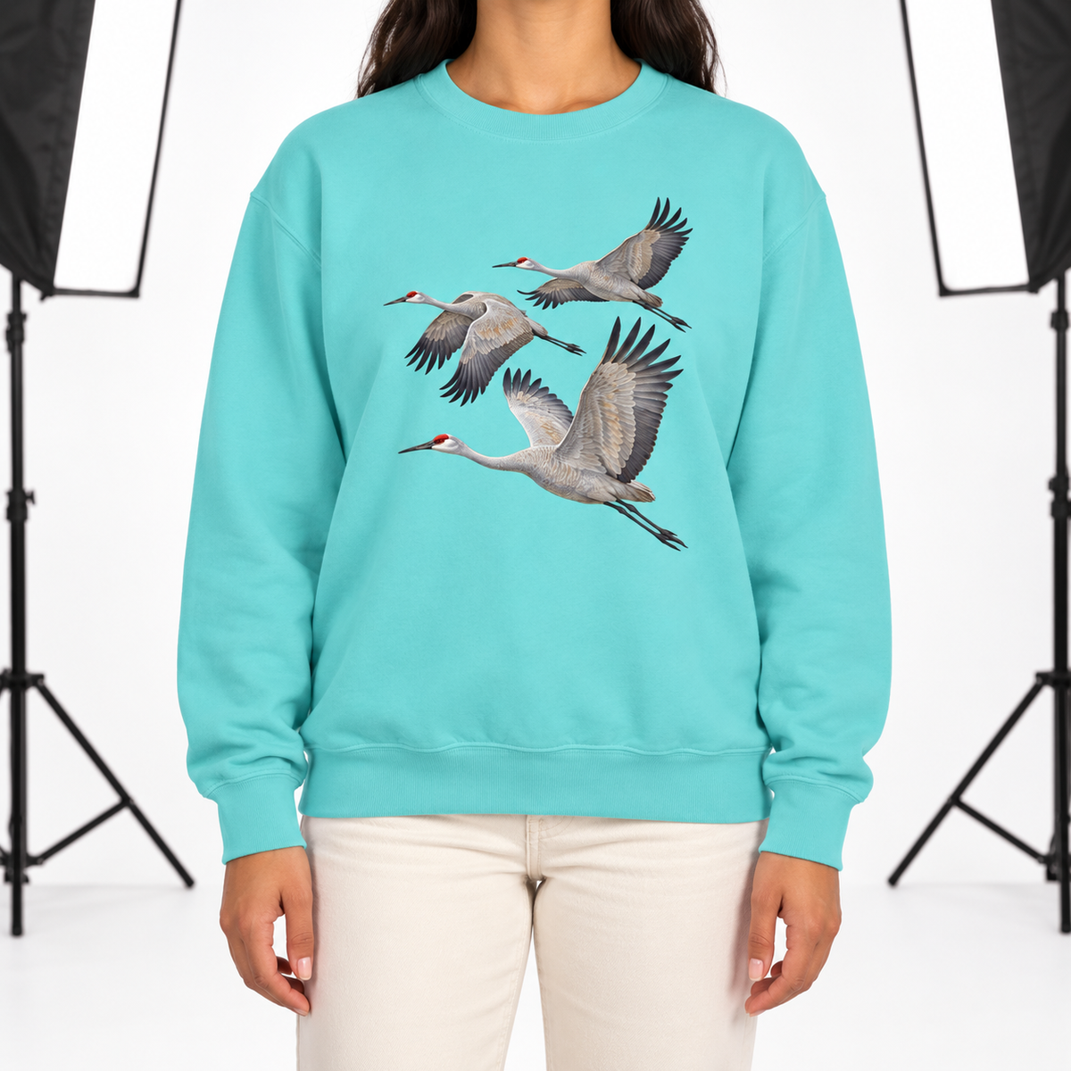 Woman wearing a Chalky Mint Comfort Colors 1566 crewneck sweatshirt with three sandhill cranes in flight printed on the chest, no text
