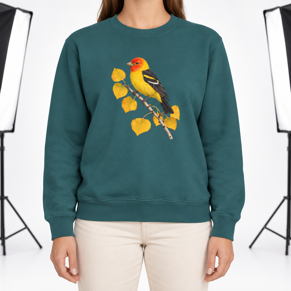 Woman wearing the Western Tanager on Golden Aspen sweatshirt in Blue Spruce, a yellow tanager with a red head on a branch of golden aspen leaves, large centered chest print